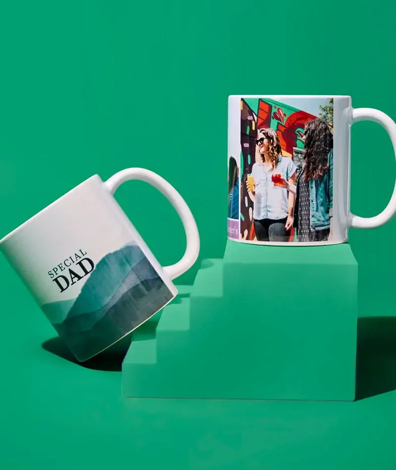 Two personalised photo mugs displayed on green steps, one featuring a Special Dad design and the other showing a printed photo against a bright green background.